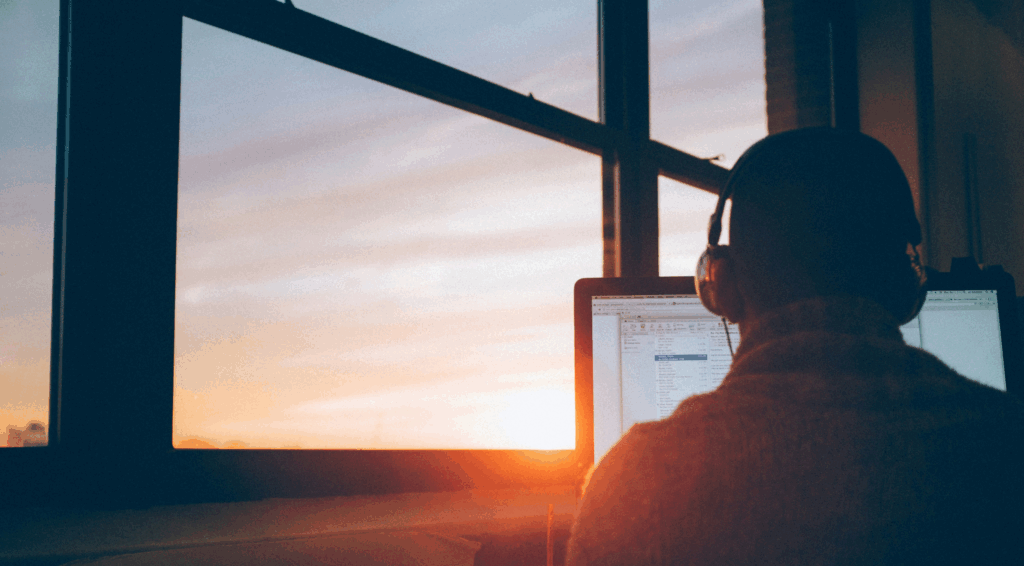 Entrepreneur working on a computer with headphones during sunset, symbolizing remote work, focus, and innovation.